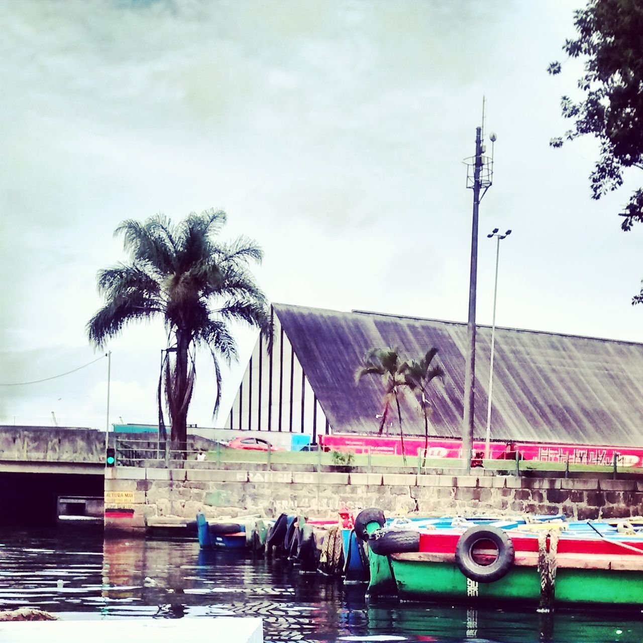 palm tree, architecture, built structure, building exterior, sky, transportation, water, tree, cloud - sky, city, mode of transport, nautical vessel, sea, incidental people, cloud, cloudy, outdoors, day, waterfront, car