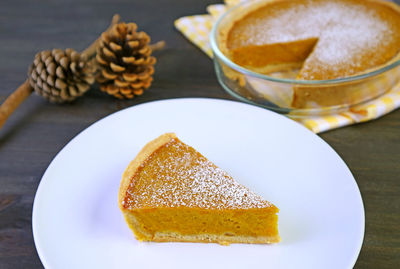 A slice of homemade pumpkin pie with blurry whole pie for the concept of autumn and thanksgiving