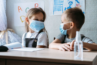 Back to school safety. schoolkids wearing masks and using antiseptic in classroom at school