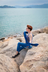 Side view of man sitting on rock at beach