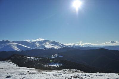 Scenic view of snowcapped mountains against sun
