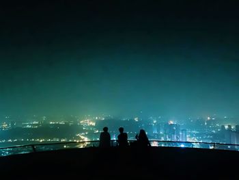 Silhouette people by railing against illuminated sky at night