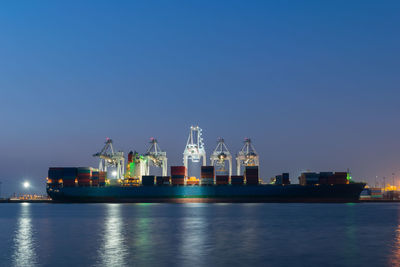 Illuminated container ship in sea against sky