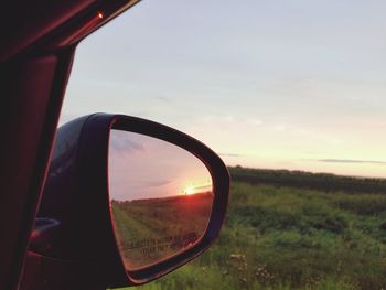 Close-up of side-view mirror on field during sunset