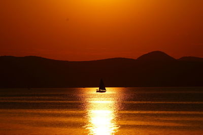 Silhouette person on sea against orange sky