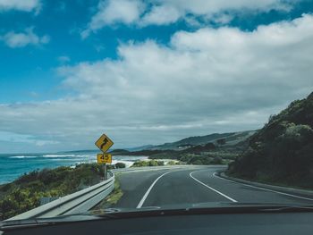 Road against cloudy sky seen through car windshield