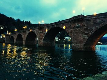Arch bridge over river against sky in city at night