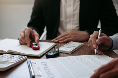 Cropped hands of customer signing contract with car salesperson sitting at desk