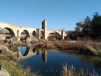 Reflection of bridge on water against clear blue sky