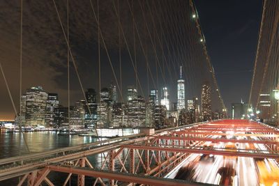 Low angle view of illuminated bridge and buildings against sky at night