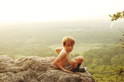 Portrait of shirtless boy sitting on mountain against clear sky