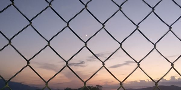 Full frame shot of chainlink fence against sky during sunset