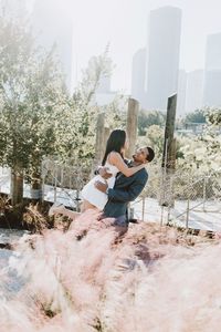 Couple embracing by fence against trees