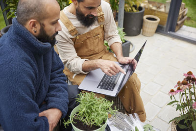 Smiling men using laptop in greenhouse