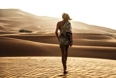 Rear view of woman walking on sand dune