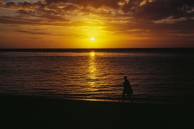 Silhouette person walking at beach against orange sky during sunset