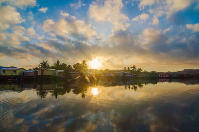 Scenic view of lake by buildings against sky during sunset