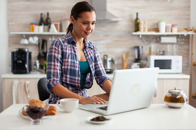 Side view of young woman using laptop on table