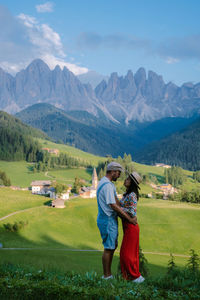 Rear view of couple standing on field against mountains