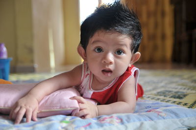 Cute baby boy looking away while lying on floor at home