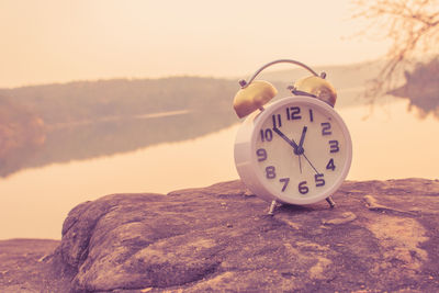 Alarm clock on cliff against lake