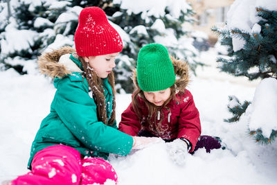 Wintertime. cute girls playing with snow, building an igloo. siblings having fun outside on snow day