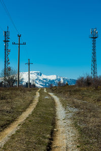 Road amidst field against clear blue sky