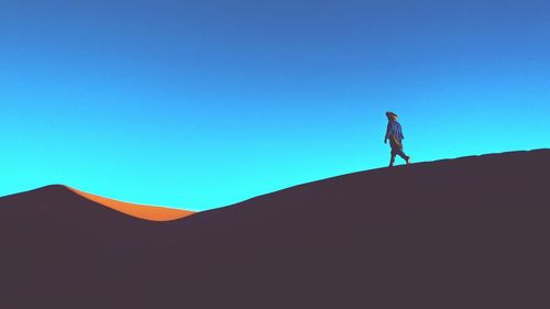 Man walking on sand dune against clear blue sky
