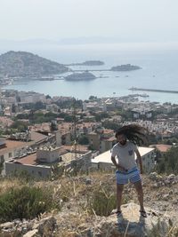 High angle view of man standing on rock against sea and sky in city