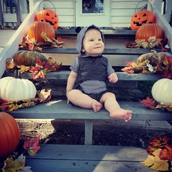 Full length of cute girl sitting by pumpkins