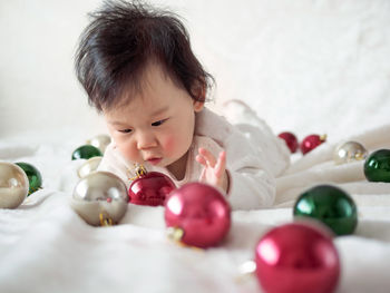 Cute baby girl lying on bed with christmas ornaments at home