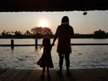 Rear view of women standing by lake against sky during sunset