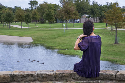 Rear view of woman sitting on retaining wall in park