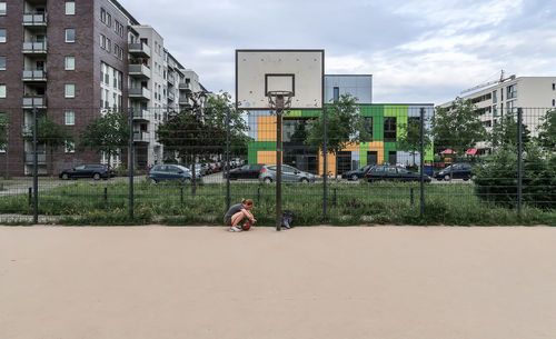 Woman with ball crouching at basketball court against sky
