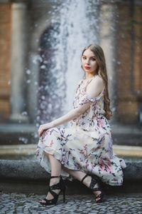 Portrait of beautiful young woman sitting against fountain in city