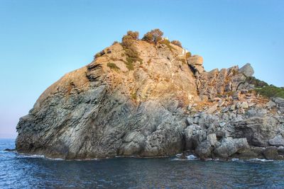 Rock formation in sea against clear blue sky