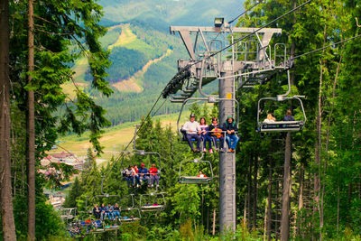 Low angle view of people sitting in ski lift amidst trees