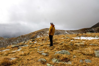 Side view of young man standing on mountain against sky during foggy weather