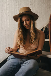 Young woman wearing hat sitting against wall