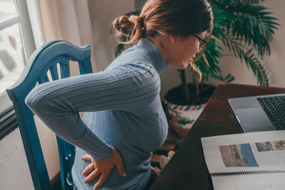 Rear view of woman using digital tablet while sitting on sofa at home