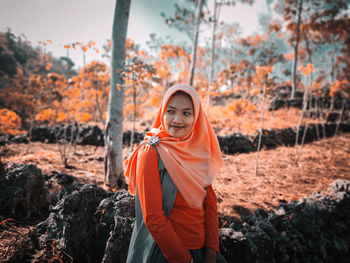 Portrait of young woman standing by trees during autumn