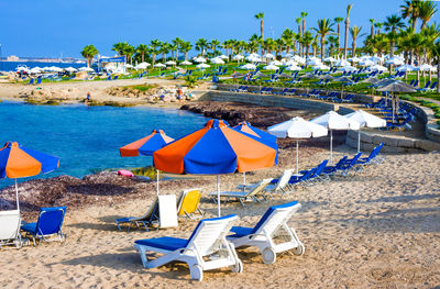 Deck chairs and parasols on beach against blue sky