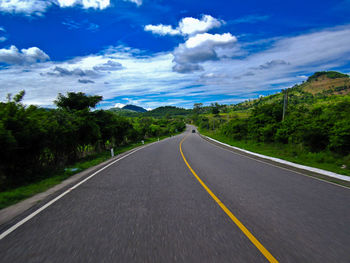 Empty road along trees and plants against sky