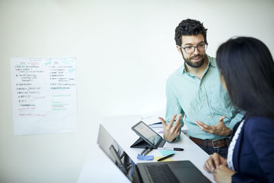 Colleagues discussing business plan while standing at desk against wall in office