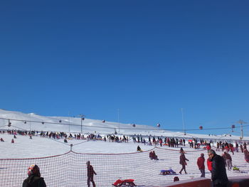 People on snow covered landscape against clear blue sky