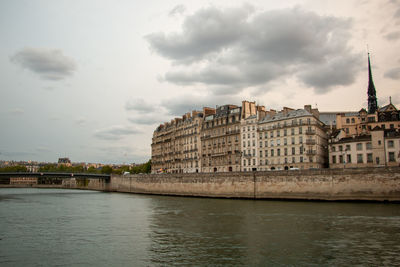 View of buildings by river against cloudy sky