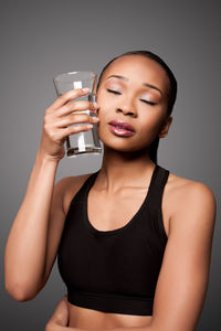 Close-up of young woman holding drink against black background