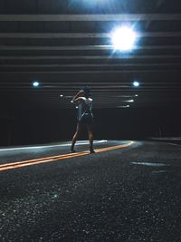 Rear view of woman standing on road under bridge at night