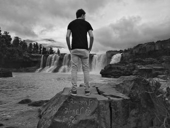 Rear view of man standing on rock against sky