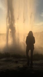 Rear view silhouette of woman standing by hot spring against sky during sunset